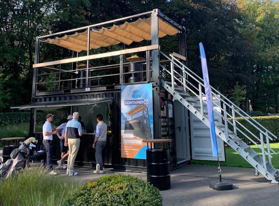 Custom branded 20 foot Mobile Rooftop bar container at Royal Antwerp Golf Club for golf tournament event  by ContainerID with custom blue branding banner and flags